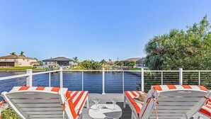 A deck with lounge chairs and a table, overlooking a body of water and a residential area. - Stunning Waterfront Oasis - Bikes, Kayaks, Pool & Spa, and much more! - Villa X-Ta-Sea - Roelens (Cape Coral)