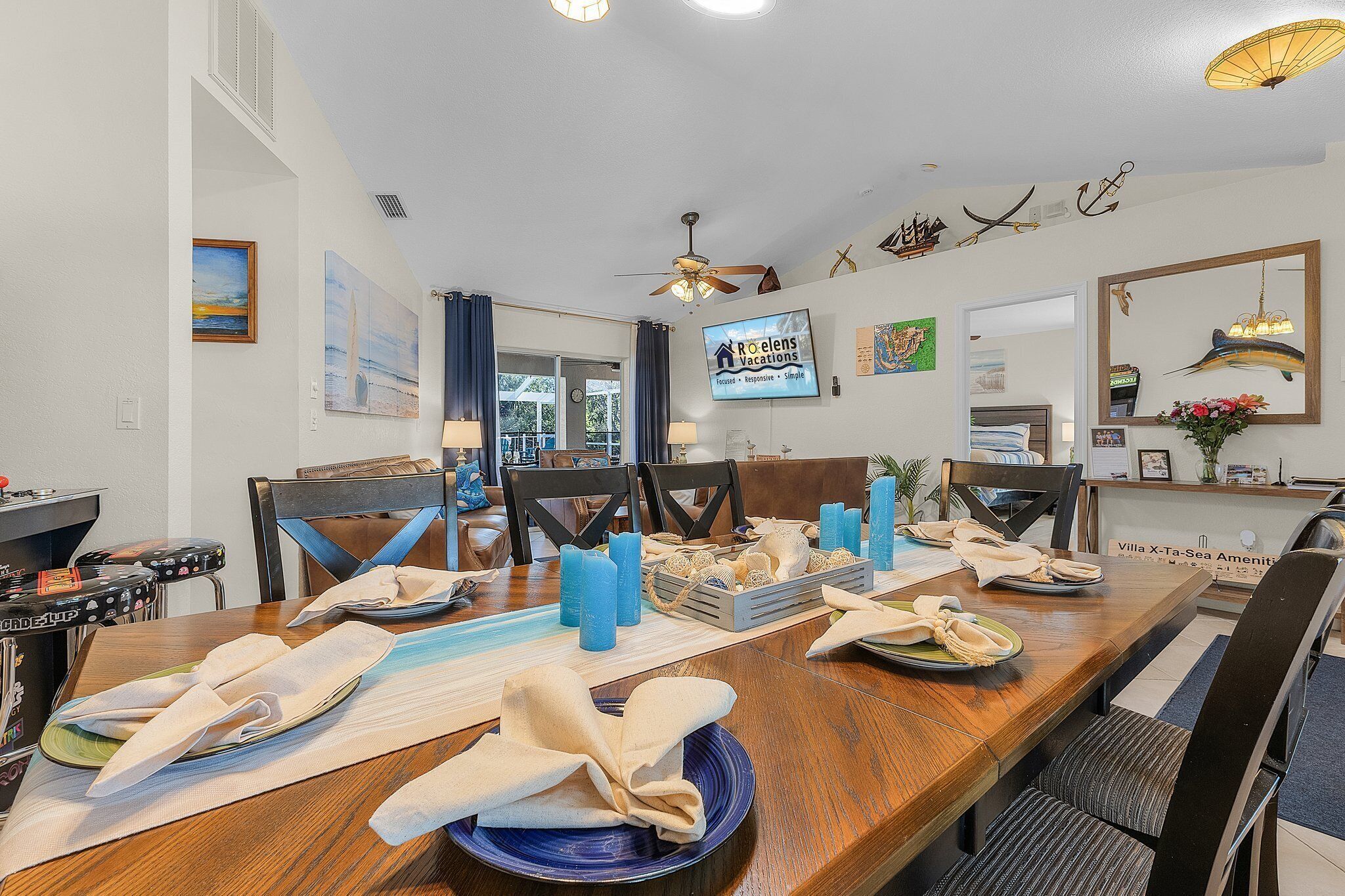 A dining area with a wooden table set for a meal, a TV mounted on the wall, and a reception desk with a sign.
