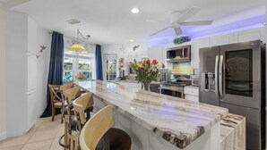 A modern kitchen with a central island, bar stools, stainless steel appliances, and a ceiling fan. - Stunning Waterfront Oasis - Bikes, Kayaks, Pool & Spa, and much more! - Villa X-Ta-Sea - Roelens (Cape Coral)