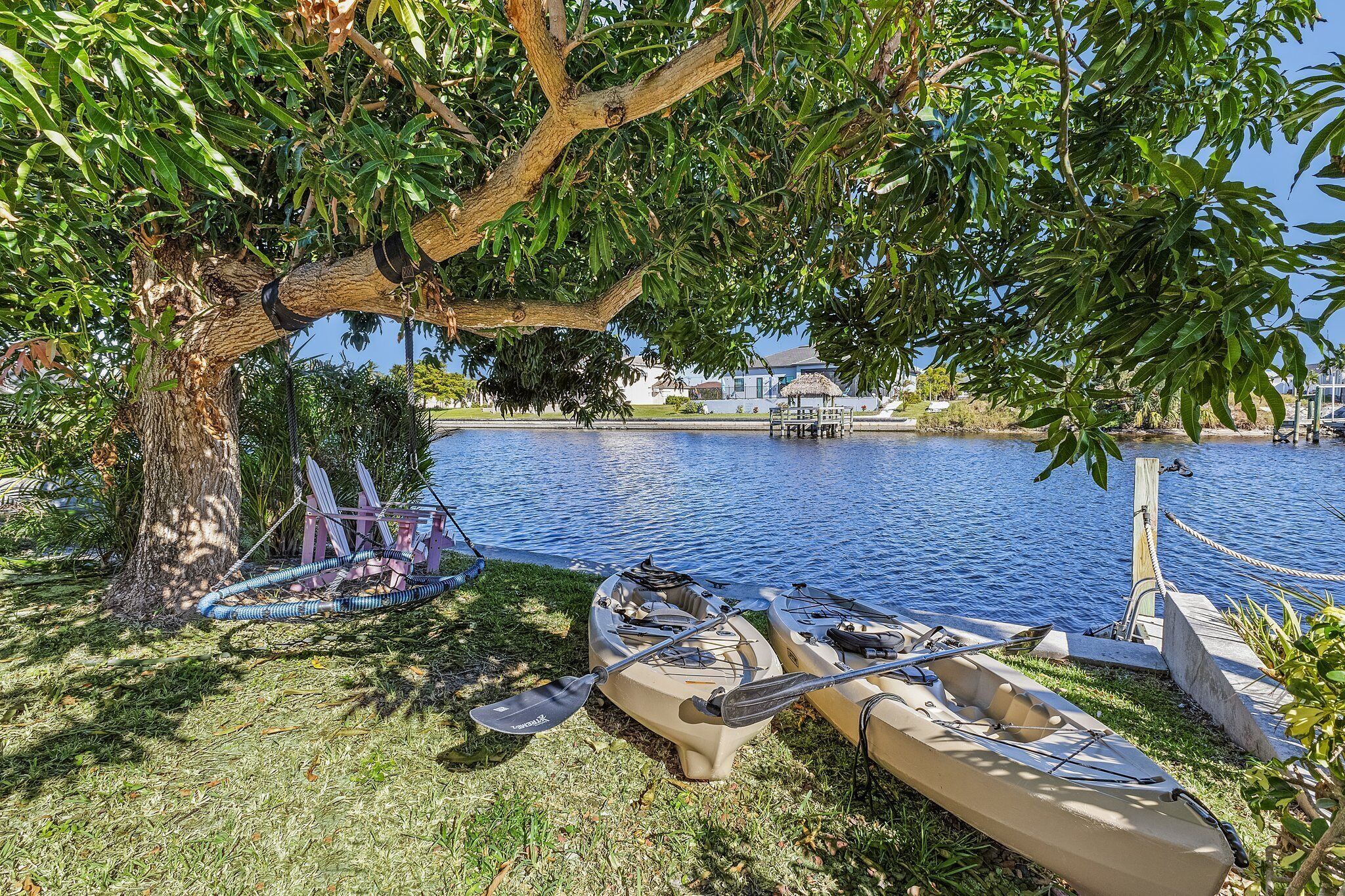 A tree-lined lakeside area with kayaks and a paddleboard docked near the water's edge.