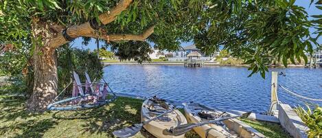 A tree-lined lakeside area with kayaks and a paddleboard docked near the water's edge.