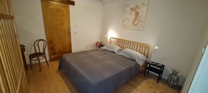 Un dormitorio con una cama de madera, una mesita de noche, una silla, una puerta de madera y un cuadro con una sirena en la pared.