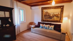 A cozy living room with a sofa, a wicker chair, a wooden cabinet, and a large framed painting on the wall. - Three Mermaids House, Piran (Piran)