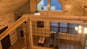 A wooden cabin with a sloped ceiling, a stone wall, and a window. - Cozy Cabin With Fire Pit and Private Hot Tub (Gatlinburg)
