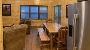 A cozy cabin interior with a wooden dining table, a sofa, and a refrigerator. - Cozy Cabin With Fire Pit and Private Hot Tub (Gatlinburg)