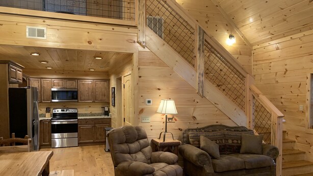 A spacious wooden cabin interior with a kitchen, dining area, and a staircase. - Cozy Cabin With Fire Pit and Private Hot Tub (Gatlinburg)