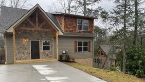 A two-story house with a stone facade, a large front porch, and a garage. - Cozy Cabin With Fire Pit and Private Hot Tub (Gatlinburg)