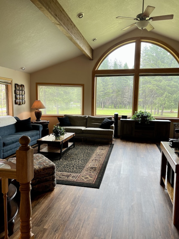 A spacious living room with a large arched window, a ceiling fan, and a wooden floor.