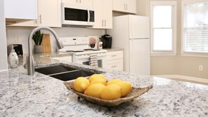 A kitchen with white cabinets, a stainless steel sink, a microwave, a stove, and a refrigerator. There is a basket of lemons on the counter.