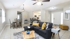 A modern living room with a dark gray sectional sofa, a wooden coffee table, and a dining area with a wooden table and chairs.