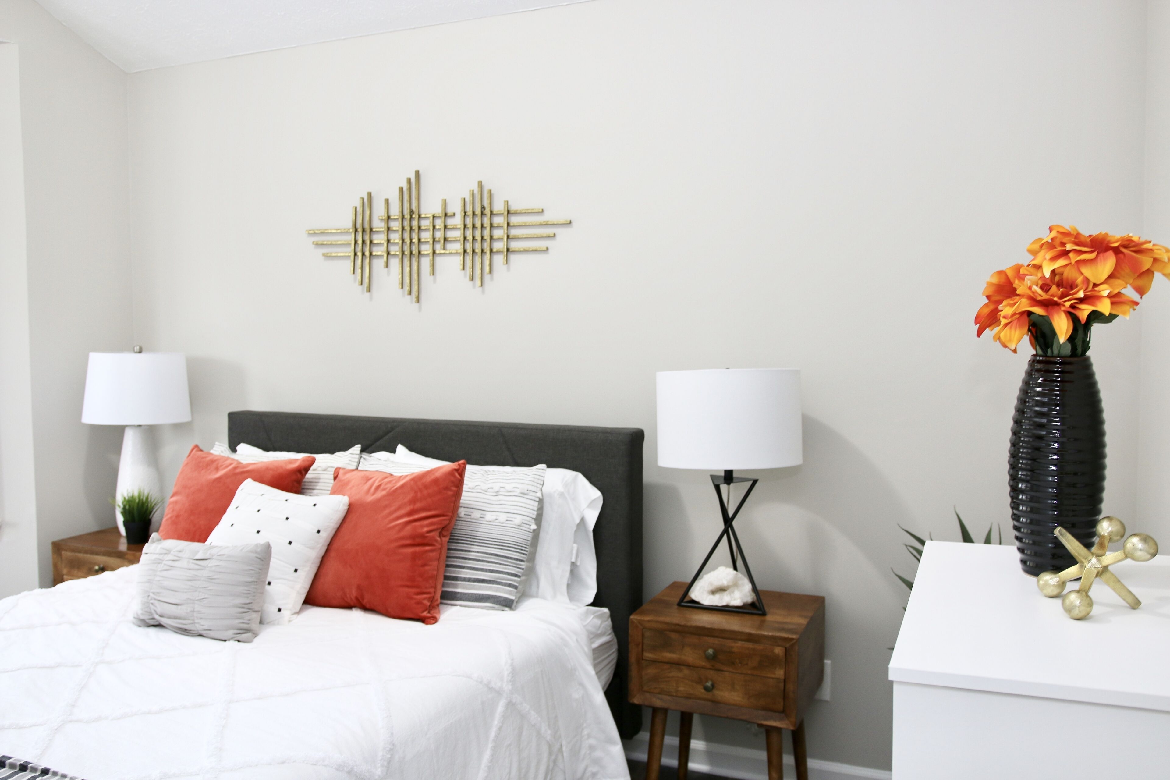 A neatly arranged bedroom with a bed, bedside tables, and a decorative wall piece.