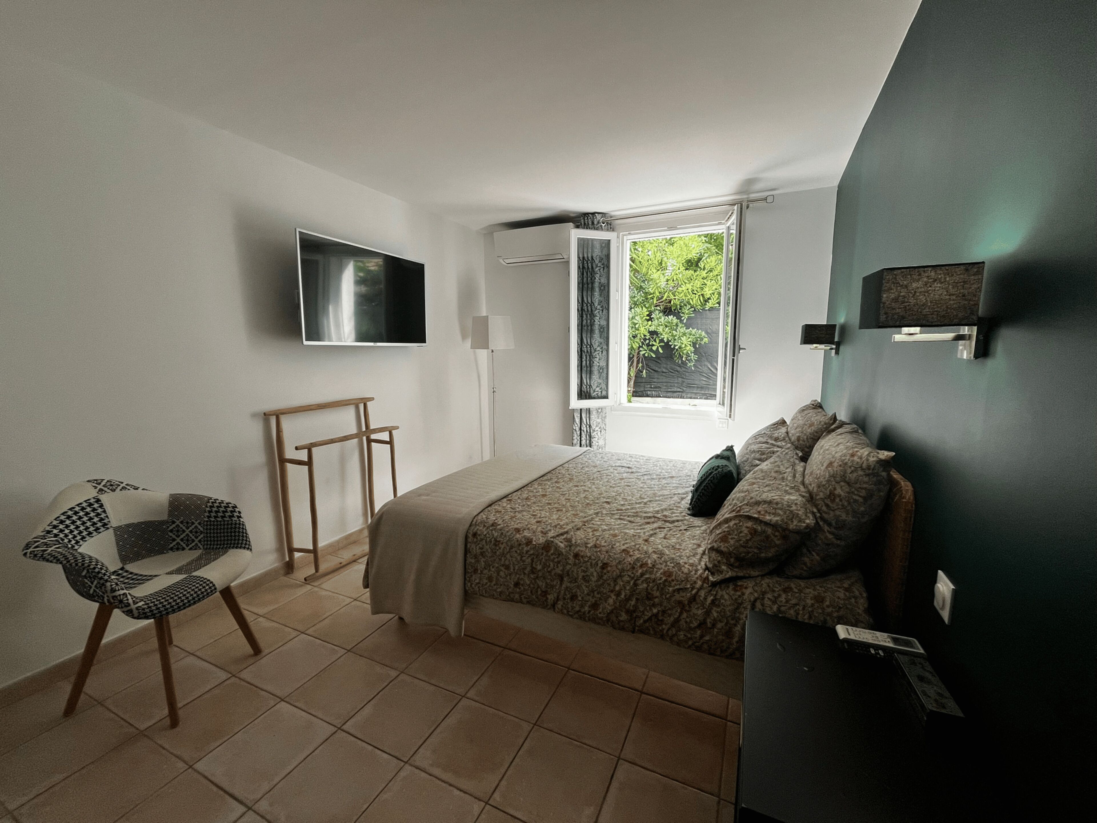 A bedroom with a bed, a chair, a TV, a window, and a door.