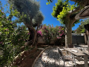 En udendørs terrasse med stenbelægning, et træbord og stole.