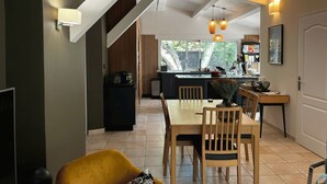 Una cocina moderna con una isla central, un comedor con muebles de madera y una escalera que lleva a un nivel superior.