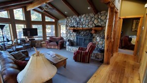 Ein gemütliches Blockhaus-Interieur mit Kamin aus Naturstein, Holzbalken und großen Fenstern.
