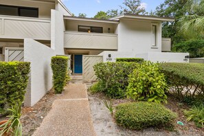 A two-story residential building with a blue door, numbered 3033 and 3034, surrounded by well-maintained hedges and a gravel pathway.