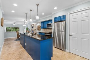 A modern kitchen with blue cabinets, stainless steel appliances, and pendant lighting.