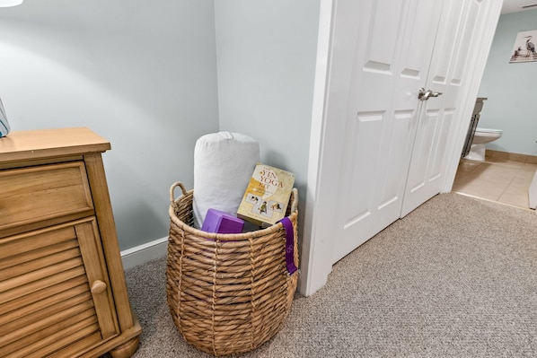 A room with a wooden cabinet, a wicker basket with a yoga mat and a book, and a white door.