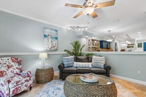 A living room with a sofa, armchair, coffee table, and a ceiling fan.