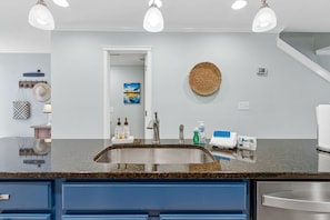 Een moderne keuken met een granieten aanrecht, een roestvrijstalen spoelbak en blauwe keukenkastjes.