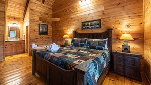Ein Schlafzimmer einer Holzhütte mit einem großen Bett, zwei Nachttischlampen, einem Nachttisch und einem gerahmten Bild an der Wand.