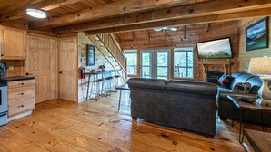 Ein großzügiger Wohnbereich mit Holzbalkendecke, einer Couch, einem Fernseher und einem Kamin.