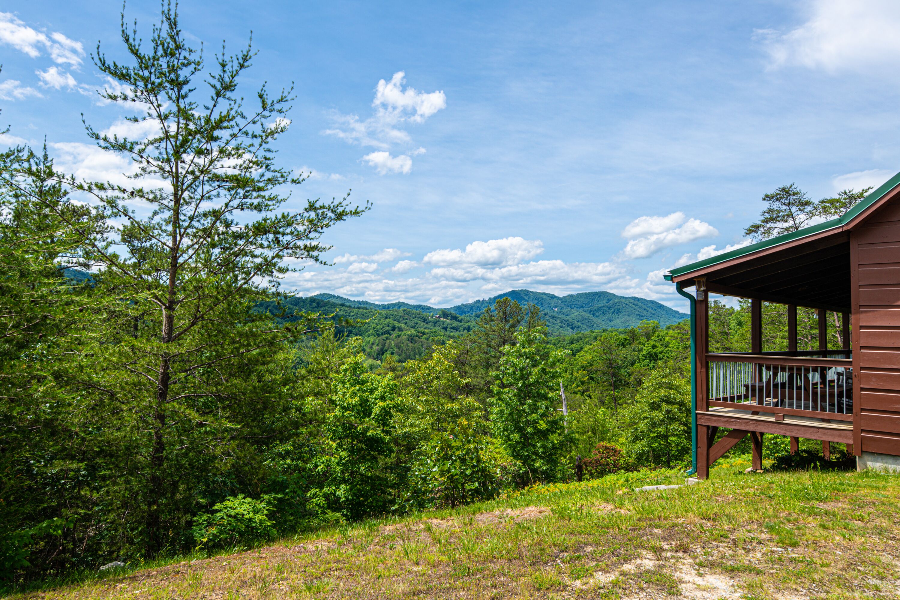 Uma cabana com varanda e vista para uma cadeia montanhosa arborizada.