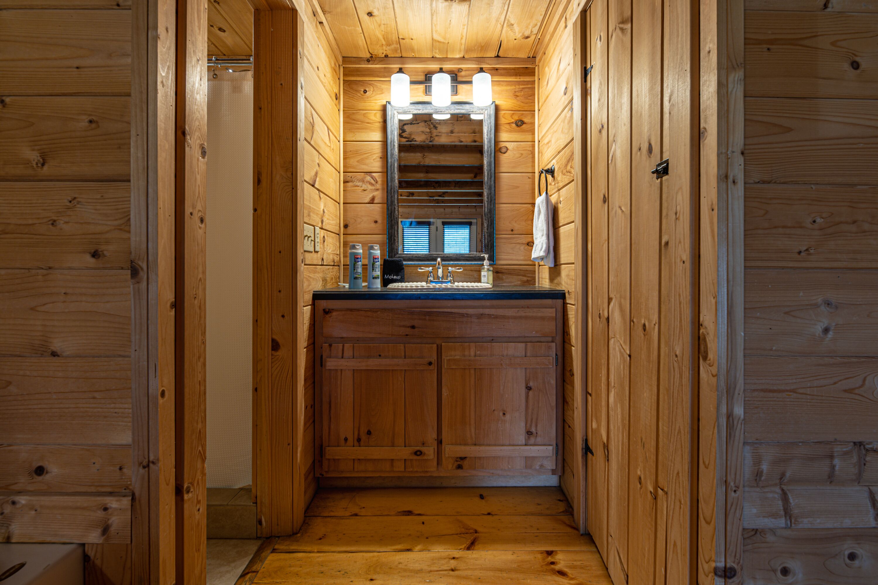 Baño de cabaña de madera con lavamanos, espejo y toalla colgada en la pared.
