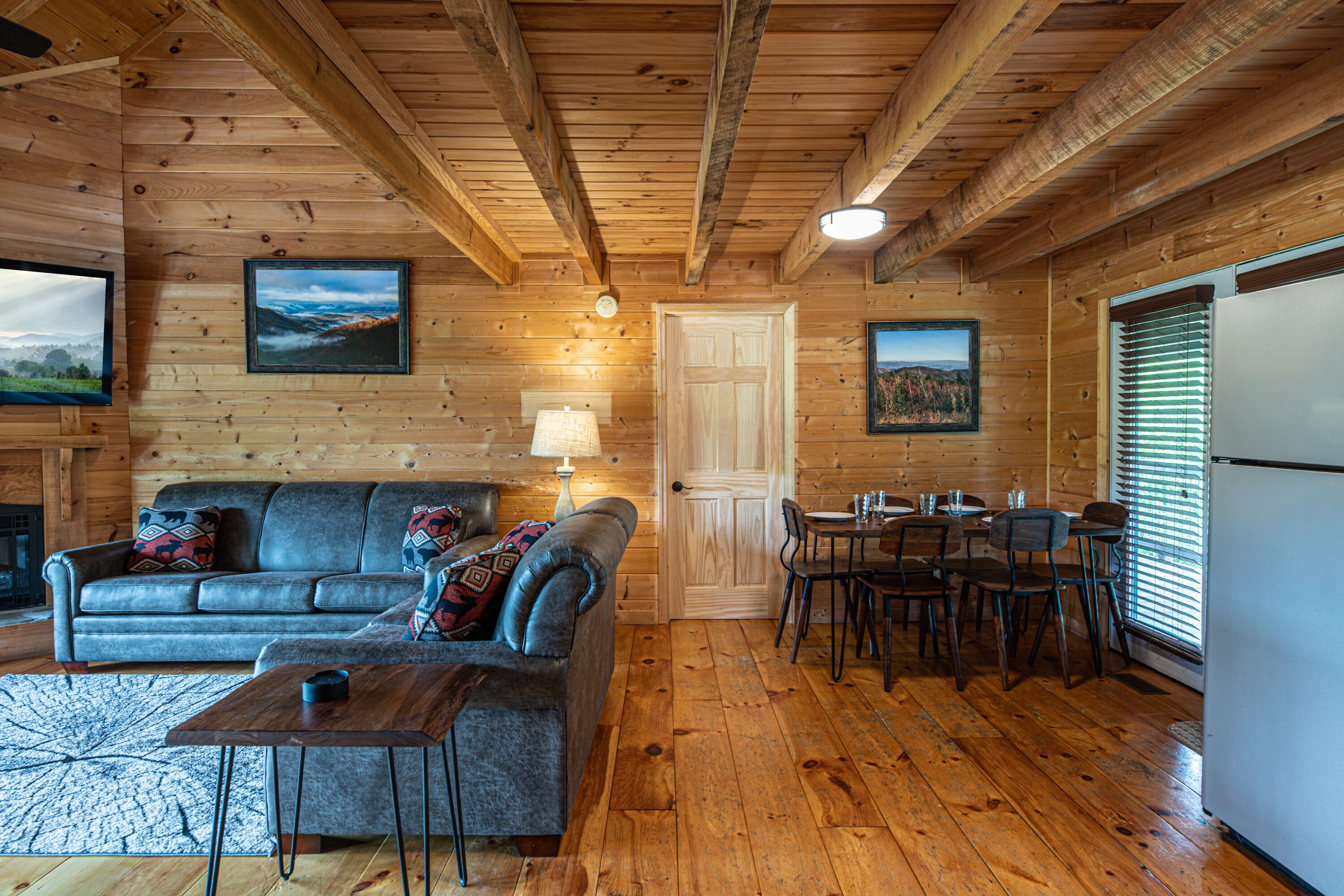 Un interior de cabaña acogedor, con paredes de madera, un sofá, una mesa de comedor con sillas y un refrigerador.