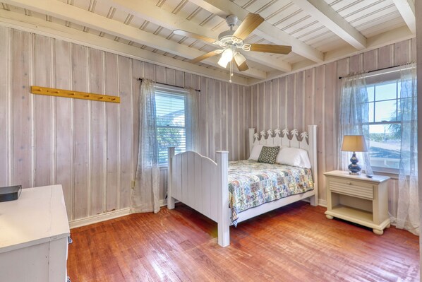 A bedroom with a wooden bed, a ceiling fan, a nightstand, and a window with curtains. - Oasis, 2nd Row Beach House, Just Steps from Beach with Beautiful Pool Area (North Myrtle Beach)