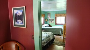Um quarto com duas camas, uma cadeira de madeira e um quadro na parede.