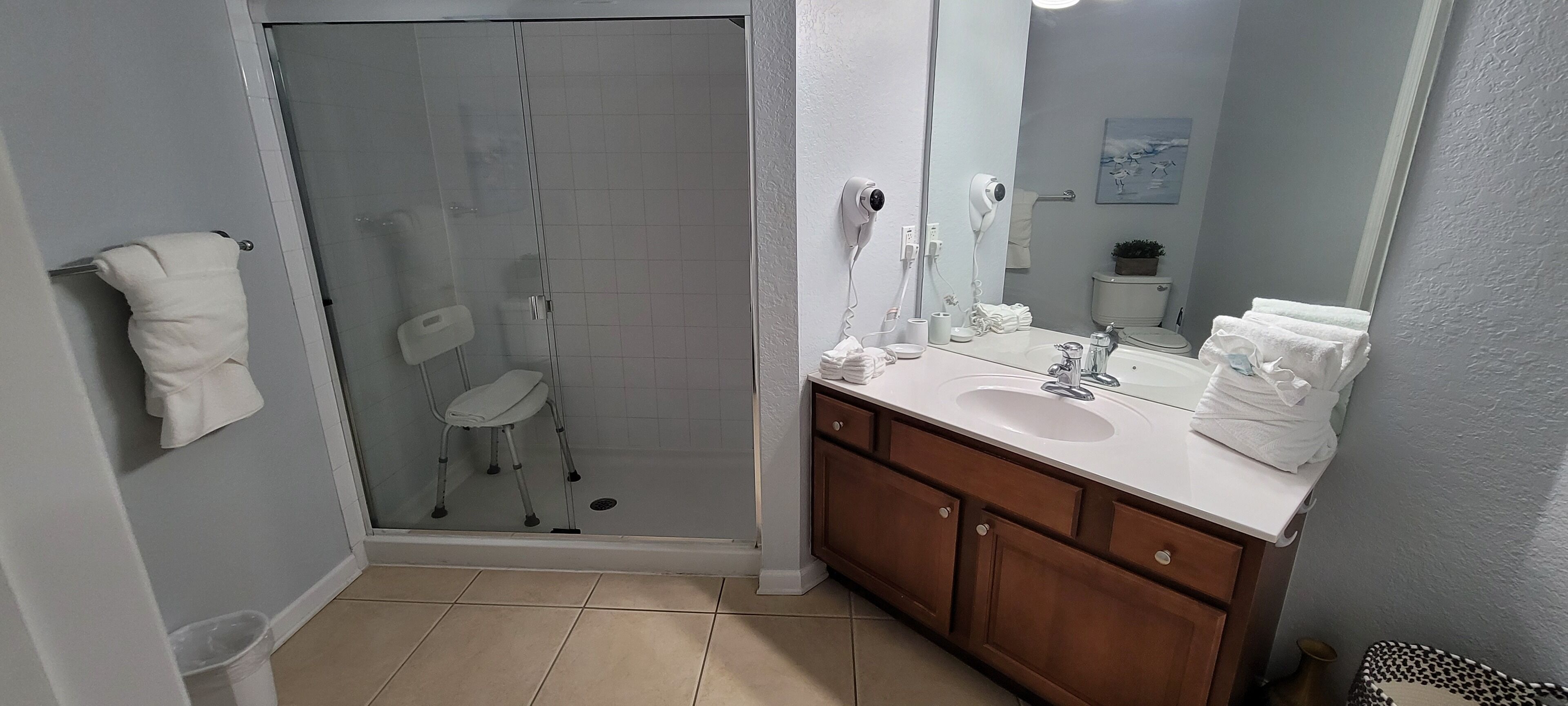 A bathroom with a glass shower enclosure, a white sink with a mirror, and wooden cabinets.