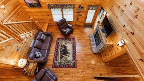 A log cabin interior with a wooden floor, a fireplace, a sofa, a coffee table, and a rug.