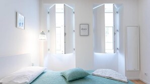 Une chambre à coucher avec un lit, deux fenêtres, une lampe de chevet et un tableau encadré au mur.