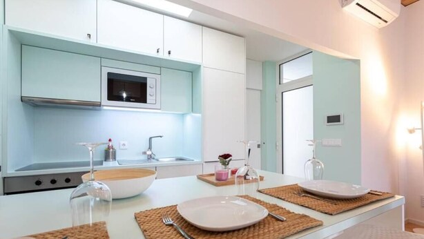 Une cuisine moderne avec des meubles blancs, un four à micro-ondes et un évier. On y trouve deux tables à manger, chacune agrémentée de sets de table et de couverts.