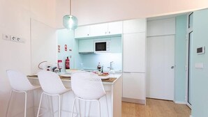 Une cuisine compacte avec des tabourets de bar blancs, un four à micro-ondes et un luminaire suspendu.