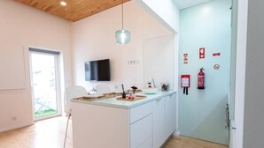 Une cuisine moderne avec un îlot central, un téléviseur fixé au mur et un extincteur sur la porte.
