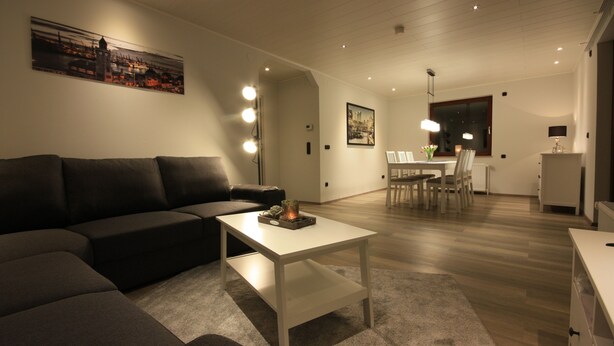 A modern living room with a sectional sofa, a white coffee table, and a dining area with chairs and a table. - Weiße Höhen - Ferienhaus, Dibbersen bei Hamburg (Buchholz in der Nordheide)