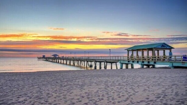 Ein Strand mit einer an das Wasser reichenden Pier, einem überdachten Sitzbereich und einem klaren Himmel.
