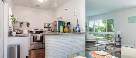 A modern kitchen with a central island, stainless steel appliances, and a dining area with glass tables and woven placemats.