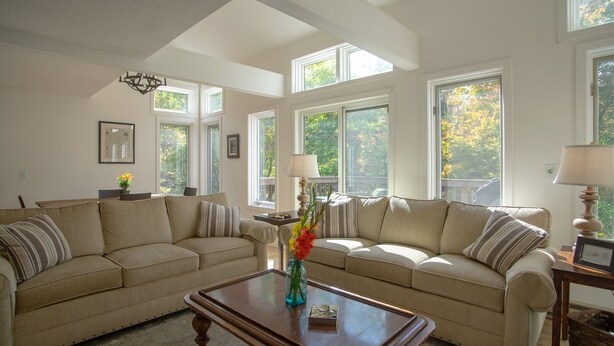 A spacious living room with two beige sofas, a wooden coffee table, and large windows offering views of trees. - 10th Hole Haystack Golf Course in Wilmington VT - 4 miles from Mt Snow (Wilmington)