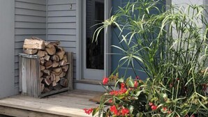 A wooden porch with steps leading to a blue door, a stack of firewood, and a potted plant with red flowers. - 10th Hole Haystack Golf Course in Wilmington VT - 4 miles from Mt Snow (Wilmington)