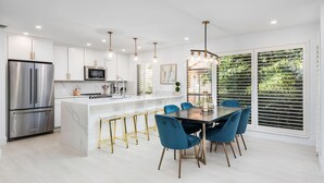 Una cocina moderna con una isla central, electrodomésticos de acero inoxidable y sillas azules alrededor de una mesa de comedor.