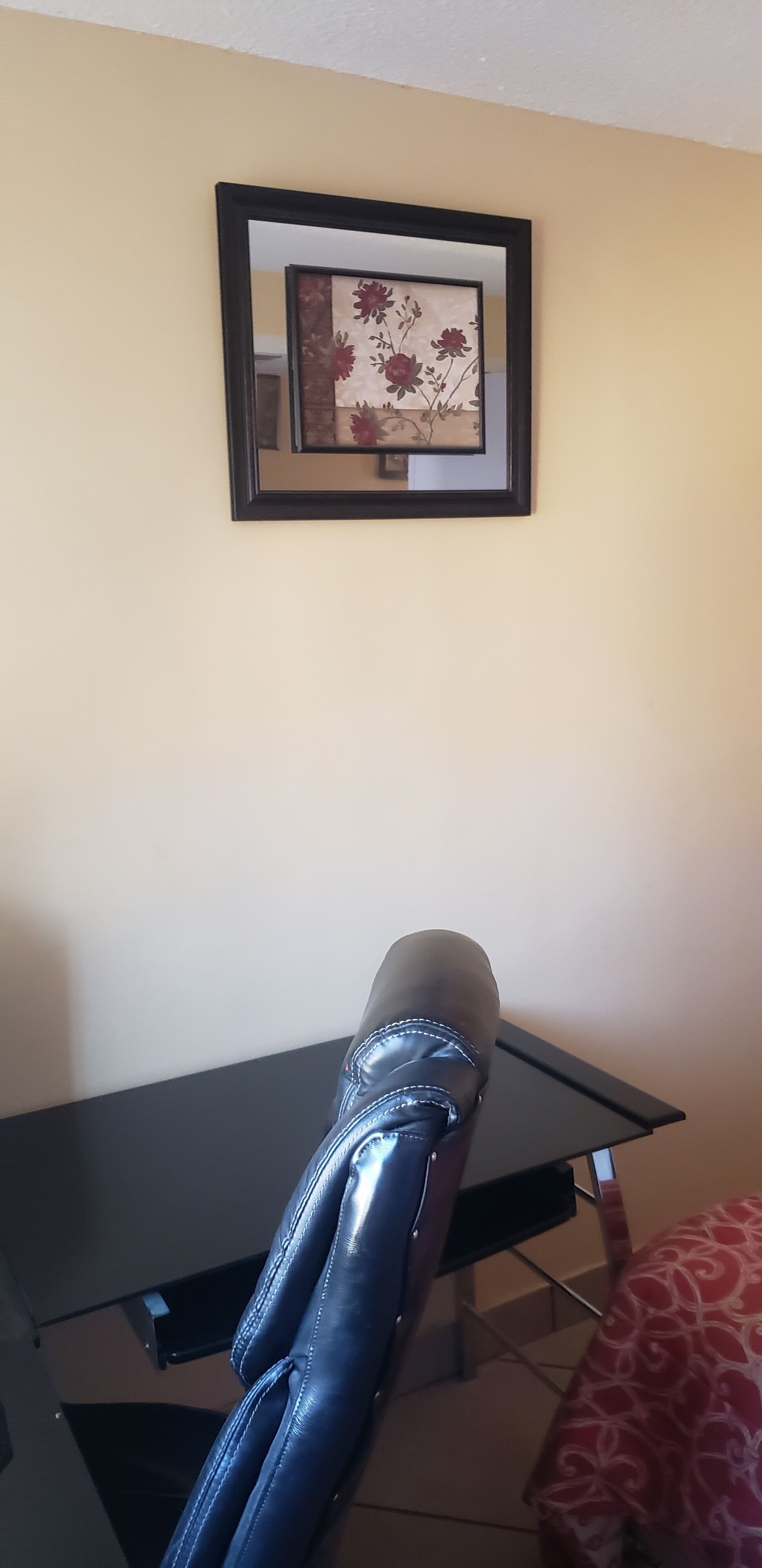 A room with a black dining table, a framed floral artwork on the wall, and a black leather chair.