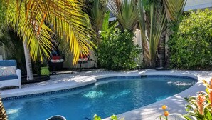 A swimming pool surrounded by lush greenery and a decorative stone urn. - Enchanted Private Island Oasis Steps To Beach, Tropical Yard & Charm Filled Home (Placida)