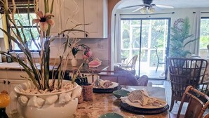 A kitchen with a granite countertop, white cabinets, and a dining area with a table set for four. - Enchanted Private Island Oasis Steps To Beach, Tropical Yard & Charm Filled Home (Placida)