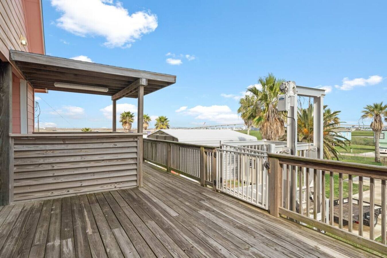 A wooden deck with a railing, overlooking a beach with palm trees and a clear sky.