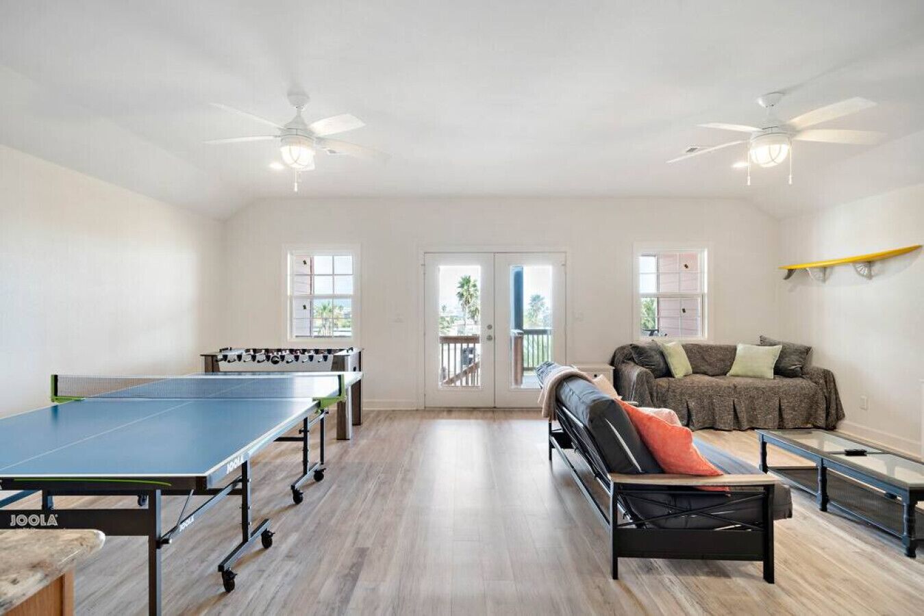A spacious living area with a ping pong table, a sofa, and a ceiling fan.