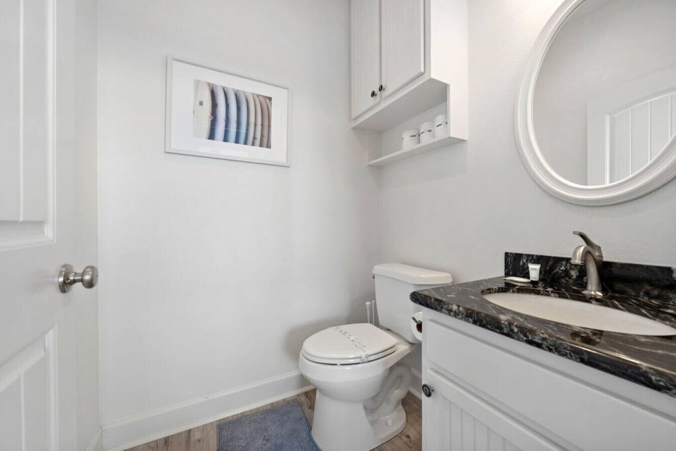 Une salle de bain avec des toilettes blanches, un lavabo doté d’un plan de travail en marbre et un tableau encadré au mur.