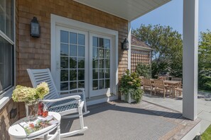 A covered patio with a rocking chair, a table with a vase of flowers, and a dining area with wooden furniture. - Newly constructed 3 BR house . Walk to town, harbor and restaurants (Nantucket)